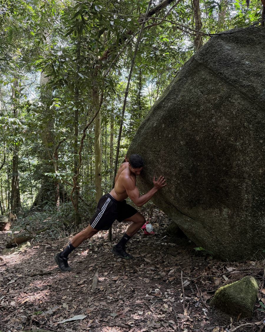 Th&eacute;o pushing against a boulder in the forest